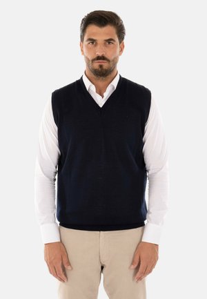 Gilet in maglia senza maniche di colore blu navy, con scollatura a V, indossato sopra una camicia bianca a maniche lunghe. Presenta una texture liscia e una forma semplice.