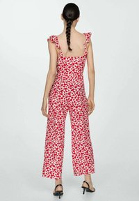 Červený květinový overal s volánovými ramínky, širokým střihem nohavic a lehkým materiálem, který má po celé ploše rozptýlený květinový vzor.
