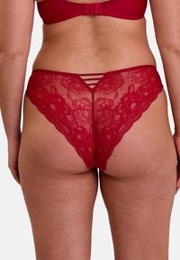 String rouge en dentelle avec motif floral, dotée d'un bord festonné et d'un détail à lanières au dos. Texture douce et transparente.