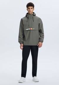 Giacca leggera verde oliva con cappuccio, design a metà zip, polsini elasticizzati e una striscia di logo bianco e colorato sulla parte superiore del petto.