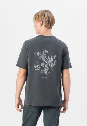 Mörkgrå bomullströja med en vit blommönstring på baksidan. Kort ärm och rundad halsringning med en avslappnad passform.
