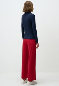 Navy-blaues, geripptes Langarmoberteil kombiniert mit lockeren roten Hosen. Das Outfit zeichnet sich durch ein minimalistisches Design und eine weiche Textur aus, ergänzt durch weiße Sneaker.