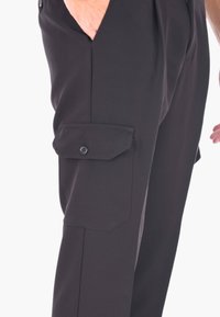 Pantaloni cargo neri con tasca laterale con chiusura a bottone, vestibilità sagomata e tessuto morbido. Design leggero e versatile.