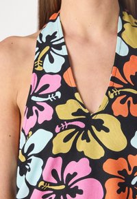 Halternekki toppi mustasta kankaasta, jossa on suuria monivärisiä hibiskuksia (vapaa, sininen, oranssi, keltainen) ja V-muotoinen kaula-aukko.