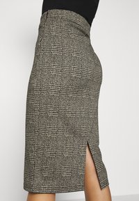 Knälång blyertskjol i svart och beige rutmönster, med en sidslits och en figurnära design med en mjuk textur.