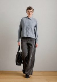 Stribet lyseblå skjorte med knapper og oversized grå denimbukser, kombineret med en sort håndtaske og sorte sko, sat mod en neutral baggrund.