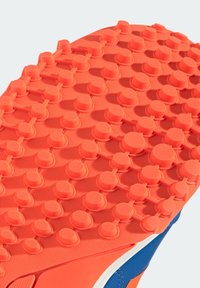 Semelle de chaussure en caoutchouc orange avec des crampons circulaires en relief reliés par de petites barres pour la traction, fixée à une partie supérieure bleue de la chaussure.