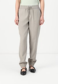 Pantalons de survêtement élastiques gris clair avec taille à cordon, poignets fuselés et poches latérales. Associés avec des chaussures noires à détail boucle.