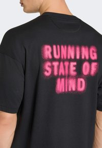 Μαύρο βαμβακερό μπλουζάκι με υπερμεγέθη ροζ κείμενο σε σπρέι "RUNNING STATE OF MIND" στην πλάτη. Κοντά μανίκια και άνετη εφαρμογή.