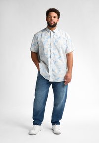 Camicetta a maniche corte con motivo floreale blu su sfondo chiaro, abbinata a jeans blu a vestibilità comoda e sneakers bianche.