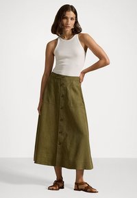 Falda khaki de botones, hecha de lino, con una cintura alta, bolsillos delanteros y una silueta larga y fluida, combinada con una camiseta ajustada blanca.