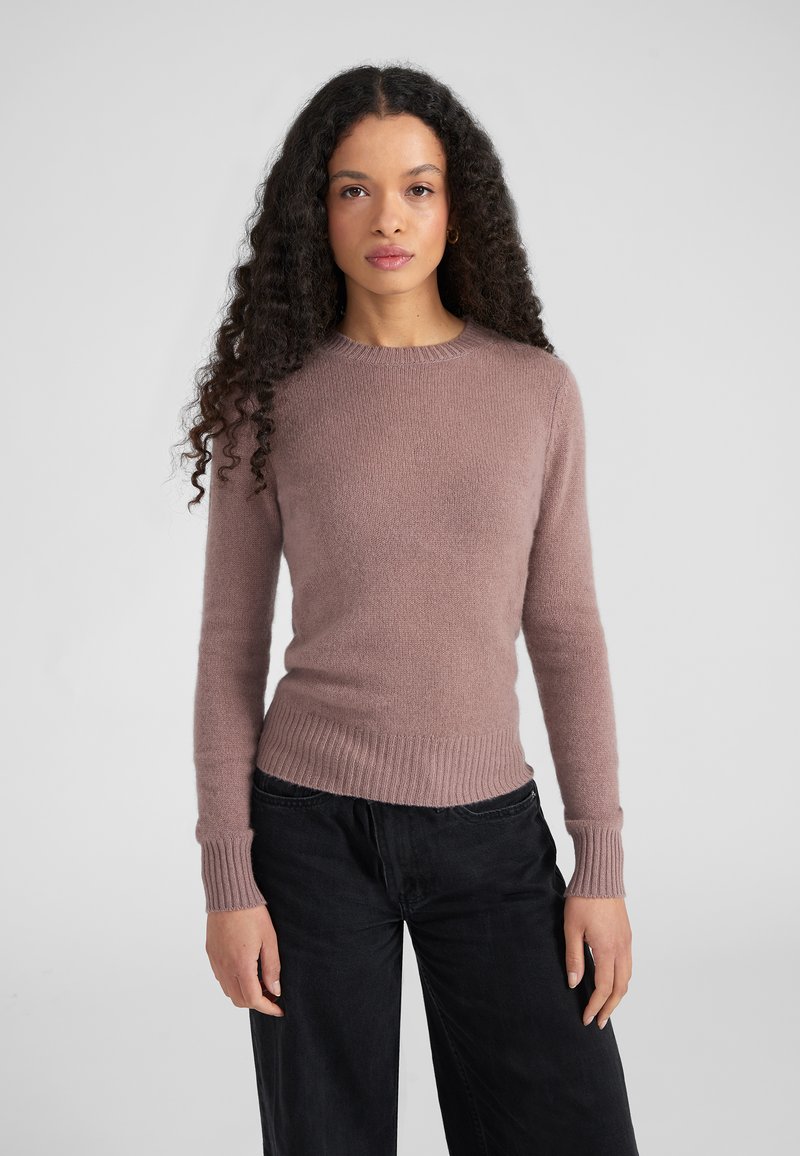 Suéter rosa claro hecho de material suave, con cuello redondo, puños acanalados y dobladillo, combinado con pantalones negros.