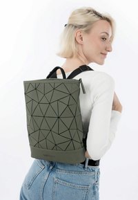 Zaino verde con motivo geometrico realizzato in materiale testurizzato, dotato di una cerniera superiore e spallacci neri a contrasto, tenuto contro uno sfondo bianco.