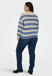Gestreepte gebreide trui in beige en blauw, met een ontspannen pasvorm, geribde manchetten en een iets langere achterkant, gecombineerd met donkerblauwe jeans en zwarte enkellaarsjes.