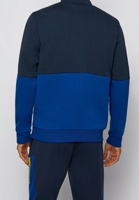 Modrá a námořnická mikina s blokovým barevným motivem, vybavená vysokým límcem, žebrovanými manžetami a lemem a hladkou texturou s čistým vzhledem.