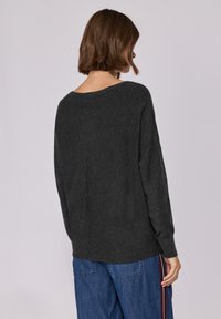 Maglione grigio scuro con una vestibilità comoda, scollatura ampia e maniche lunghe, abbinato a jeans blu con strisce laterali. Texture morbida.