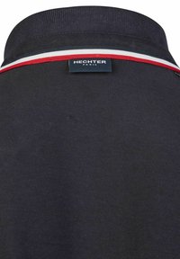 Zwarte polo met een geribde kraag en een rood, wit en blauw gestreept accent. Merktag zichtbaar aan de achterkant. Katoenen stof.