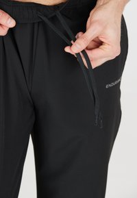 Zwarte sportbroeken met een elastische tailleband en verstelbare trekkoorden. Heeft subtiele branding op het been en een gladde textuur.