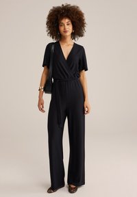 Zwarte jumpsuit met een wikkelontwerp, korte mouwen en een ceintuur in de taille. Gladde stof; ruime pasvorm, aangevuld met flats in luipaardprint.