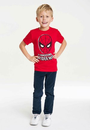 Red cotton t-shirt featuring a Spider-Man graphic on the front, paired with dark blue pants and white sneakers. Child stands confidently.