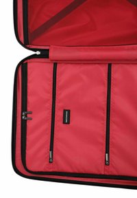 Vnitřek červené cestovní tašky se třemi zipovými kapsami, síťovanou částí a hladkým textilním podšívkou. Viditelné černé zipy a detaily štítku.
