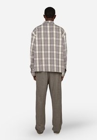 Rutete oversized skjorte i kremfarge med brune og marineblå mønstre, kombinert med grå teksturerte vidbukser. Avslappet passform, lange ermer.