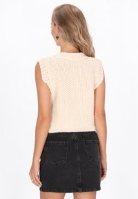 Top in maglia senza maniche di un tenue beige con un motivo testurizzato, abbinato a una minigonna in denim nero con tasche posteriori e taglio dritto.