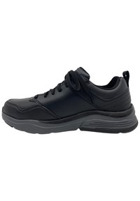 Zapatilla deportiva negra con parte superior sintética suave, punta redondeada, acentos texturizados y suela acolchada. Presenta cordones negros y una asa en la parte posterior.