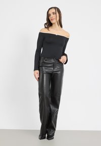 Schwarzer, schulterfreier Bodysuit mit langen Ärmeln, kombiniert mit hoch taillierten schwarzen Lederhosen mit glatter Textur und geradem Bein.