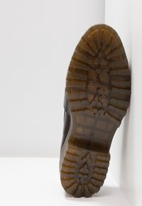 Semelle de chaussure avec une bande de roulement en caoutchouc brun translucide présentant des motifs géométriques et le numéro de taille 37 visible au centre.