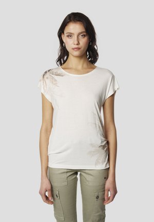 Világos bézs rövid ujjú póló puha anyagból, bal vállán pálmalevél mintával, olívazöld cargo nadrággal párosítva.