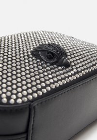 Mustalla rakenteellisella laukulla, jossa on teksturoitu pinta koristeena hopeiset niitit. Muotoiltu musta silmäteema on keskitetty etuosassa.