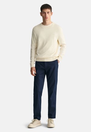 Suéter de punto beige combinado con pantalones oscuros de color marino, con una textura suave y un diseño sencillo. Zapatillas beige completan el look.