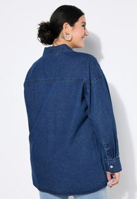 Camicia di denim di colore blu scuro, con colletto, maniche lunghe con polsini a bottoni e una vestibilità rilassata. Tessuto liscio con dettagli di cucitura.