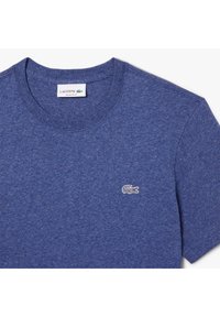 Tumma sininen crewneck t-paita, joka on valmistettu puuvillasekoitteesta. Paidassa on pieni brodeerattu krokotiililogotasku ja siitä on muotoiltu normaali istuvuus.
