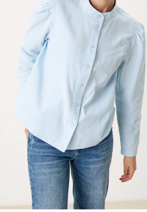 Lyseblå skjorte med knaplukning lavet af blødt stof, med en tætsiddende design, puffede skuldre og sølvknapper langs fronten.