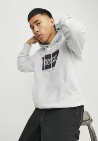 Lichtgrijze hoodie met een zwart en paars logo, capuchon met trekkoord en een voorzak. Gekocht met zwarte broek met zijritsen.