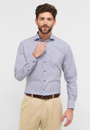 Stribet button-up skjorte i blå og hvid med lange ærmer og knapmanchetter. Den har en krave og marineblå knapper, parret med beige bukser.