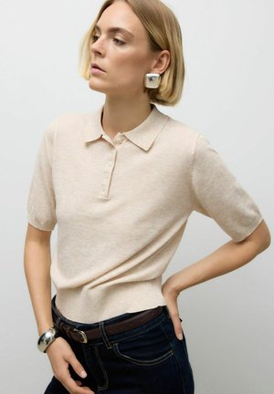 Ljust beige kortärmad polo skjorta i mjukt tyg, med krage och knappslå med fem knappar, i kombination med mörka jeans.