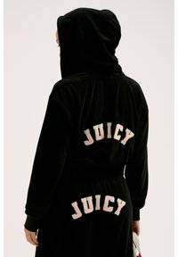 Set di felpa e pantaloni tuta in velluto nero con la scritta "JUICY" in lettere ricamate rosa e verdi sul retro. Include un cappuccio e una vita elastica.