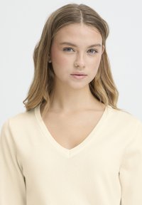 Top s výstrihom do V, na dlhé rukávy, z jemnej krémovej pleteniny s textúrovaným povrchom a mierne priliehavým strihom.