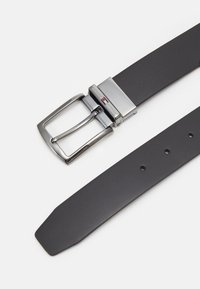 Cintura in pelle nera con fibbia rettangolare argentata. La fibbia presenta un logo decorativo e include fori per la regolazione della misura lungo la cinghia.