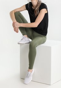 Top negro de manga corta, leggings verde oliva y zapatillas blancas. Los leggings tienen una textura suave y un ajuste ceñido.