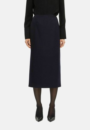 Jupe crayon bleu marine en mélange de laine, dotée d'un design mi-long avec une texture lisse, associée à des talons noires à clous et des collants.