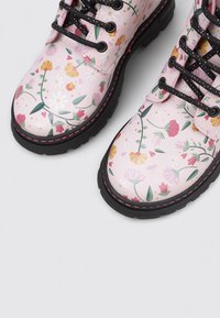 Botas rosas con cordones y suelas negras que presentan un colorido diseño floral de margaritas, tulipanes y hojas verdes.