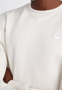 Light beige sweatshirt made of soft fabric with a crew neckline and ribbed cuffs. Features a white Nike logo on the chest.