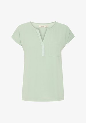 Mentazöld, rövid ujjú felső V-nyakkal és kis mellzsebbe; könnyű anyagból készült, sima textúrával.