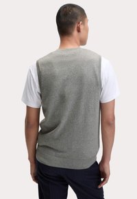 Maglione grigio senza maniche con una finitura a maglia testurizzata, orlo a costine, indossato sopra una maglietta bianca, visto da dietro.