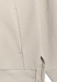 Gros plan sur un tissu beige texturé avec une couture verticale et un détail de ourlet qui se chevauche sur un vêtement.