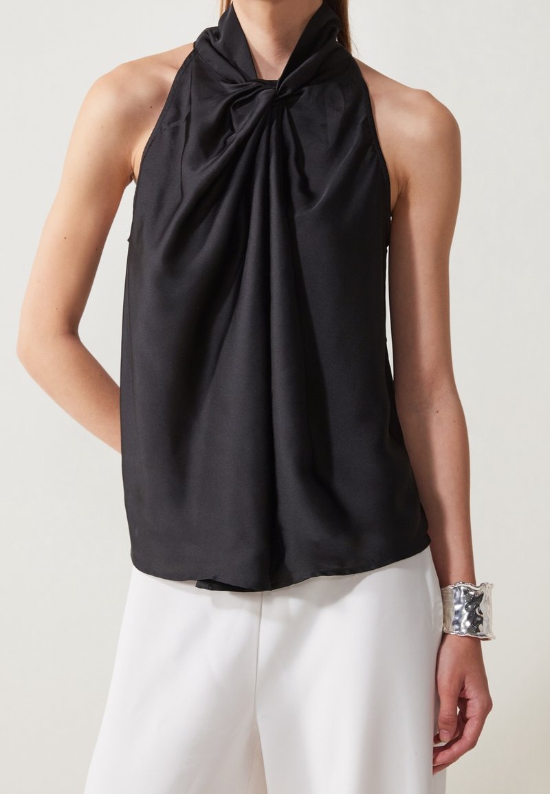 Černý saténový halter top s uzlovým designem na výstřihu, který má hladký povrch a splývavou siluetu.